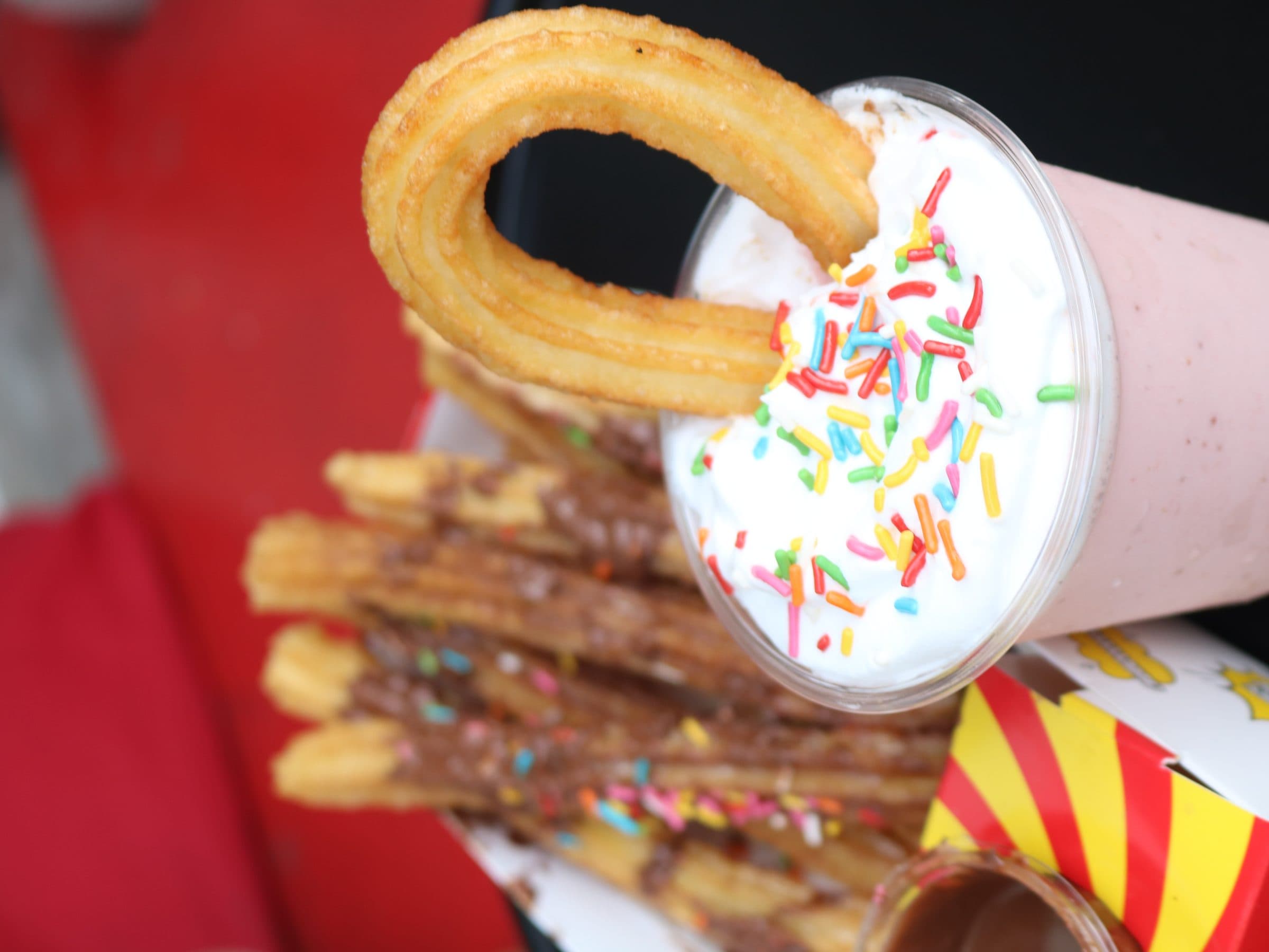 Churro dipped into a milkshake with whipped cream and sprinkles